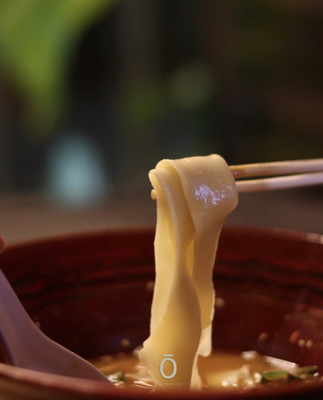 Chopsticks lifting fresh hand-pulled noodles from a steaming bowl of soup